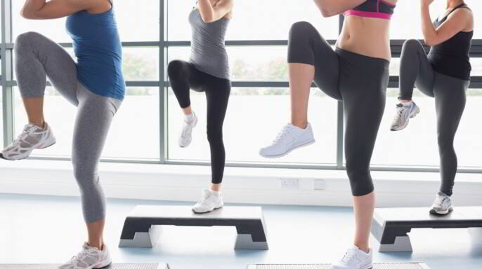 Mujeres subiendo un paso y leventando las piernas como parte de un ejercicio