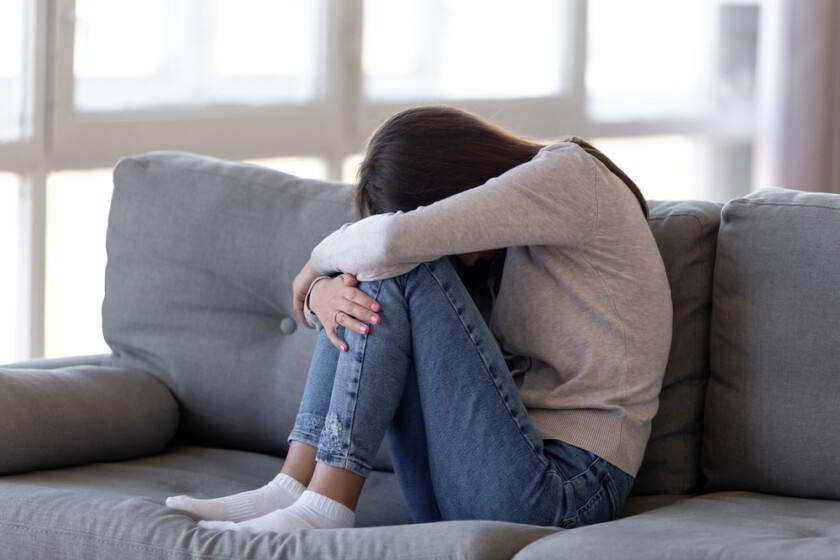 Deprimida chica adolescente sentada en el sofá sintiéndose ansiosa y sola
