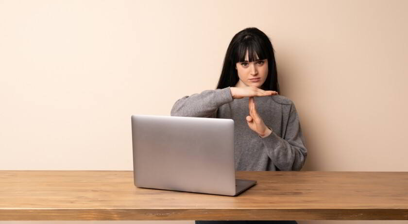 Mujer joven que trabaja con su computadora portátil haciendo con sus manos señal "T" (tiempo)