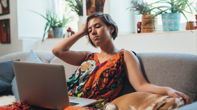 Mujer relajante en el sofá con perro usando el ordenador portátil