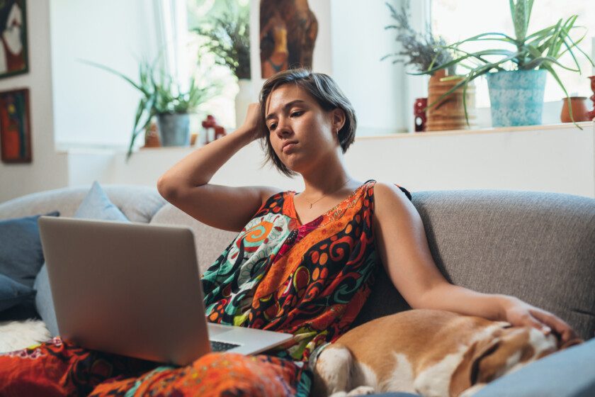 Mujer relajante en el sofá con perro usando el ordenador portátil
