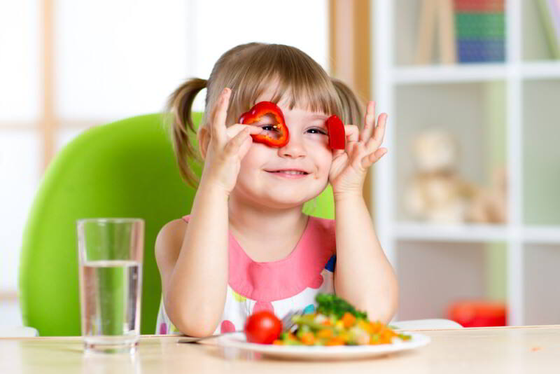 Niña divirtiéndose con verduras en la habitación de los niños