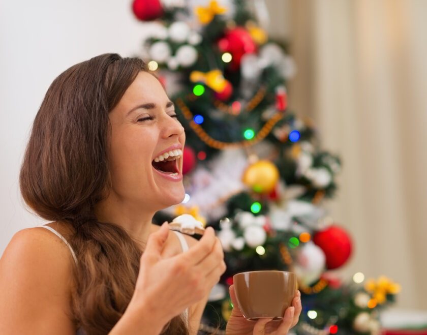 Mujer joven sonriente en pijama comiendo galletas con chocolate caliente