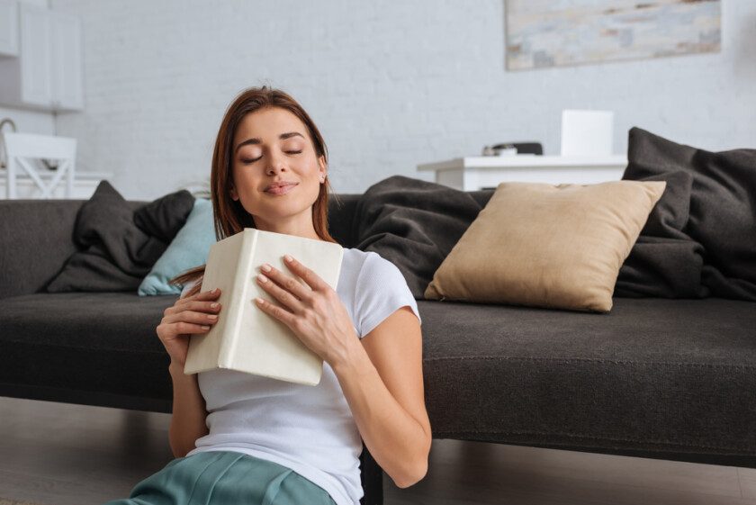 Chica de ensueño sosteniendo libro mientras está sentado en la sala de estar