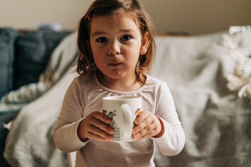 Niña caucásica bebiendo cacao de la taza en casa. Navidad