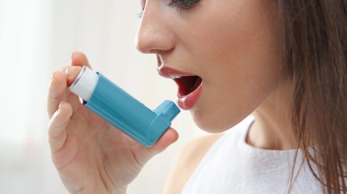 Mujer joven usando inhalador durante el ataque asmático en casa