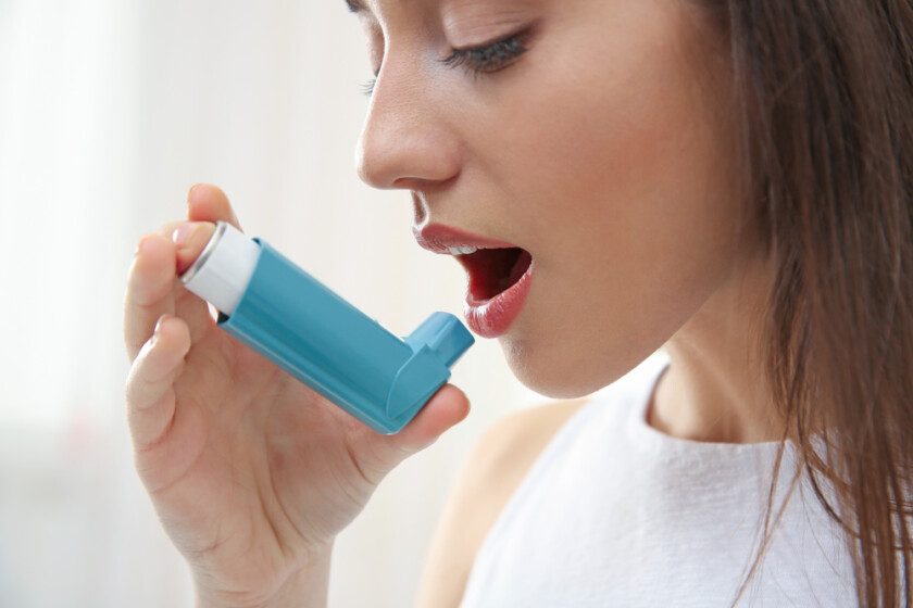 Mujer joven usando inhalador durante el ataque asmático en casa