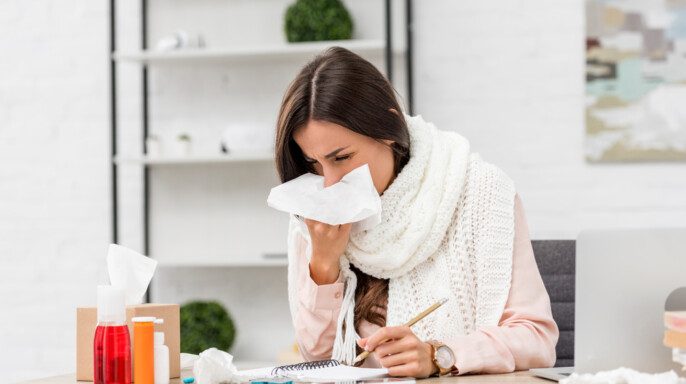 Enferma joven empresaria estornudando con servilleta de papel en el lugar de trabajo