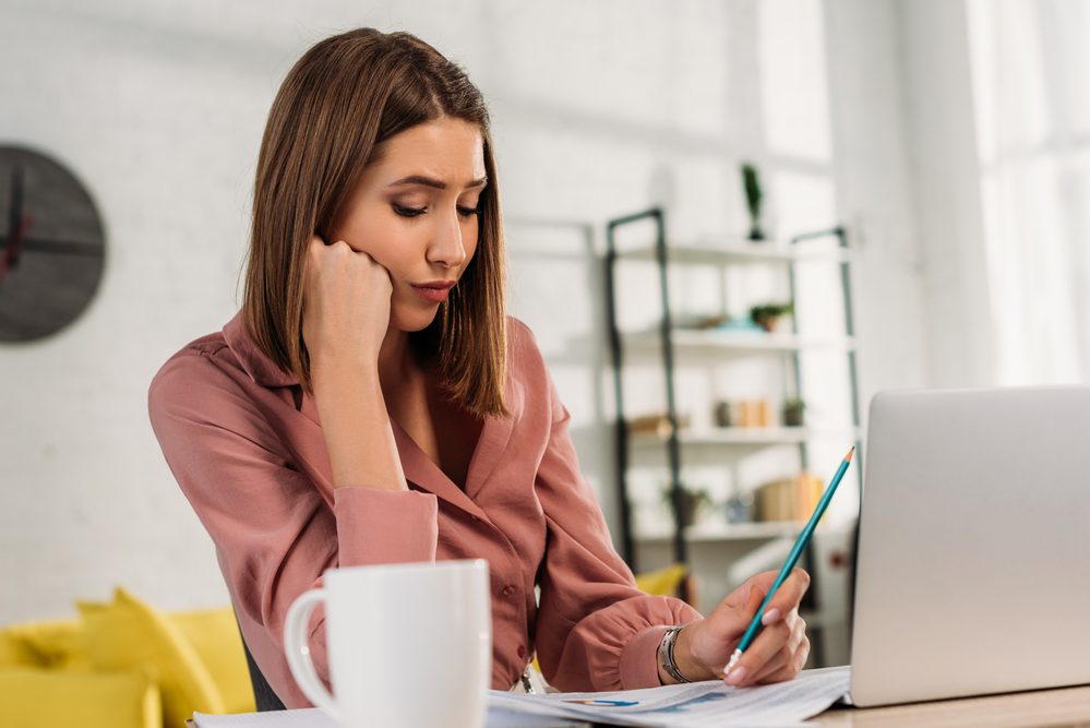 Mujer mirando gráficos y gráficos mientras sostiene el lápiz cerca de la computadora portátil en casa