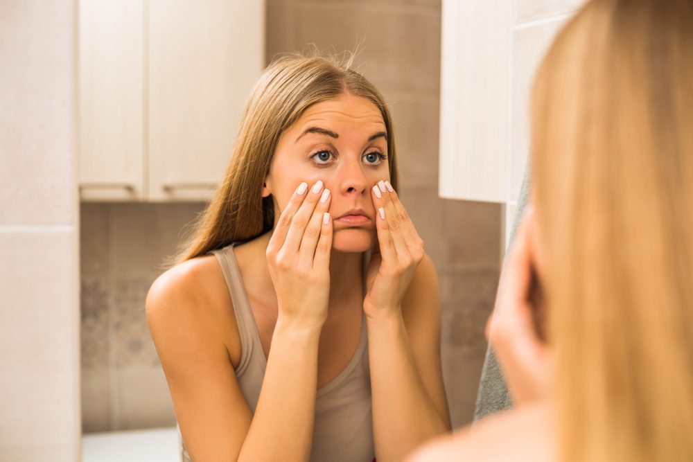 Mujer cansada mirando sus bolsas de ojos en el baño