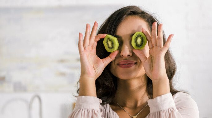 Mujer feliz sosteniendo mitades de kiwi mientras cubre los ojos