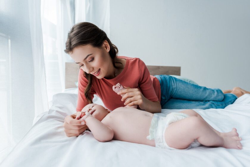 Feliz mujer tocando lindo bebé hija en dormitorio