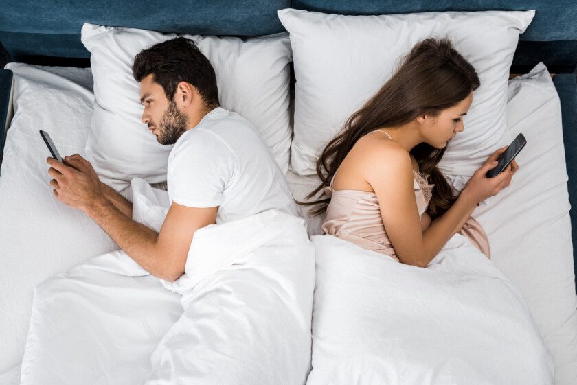 Vista superior de la joven pareja acostada en la cama por la mañana y utilizando teléfonos inteligentes