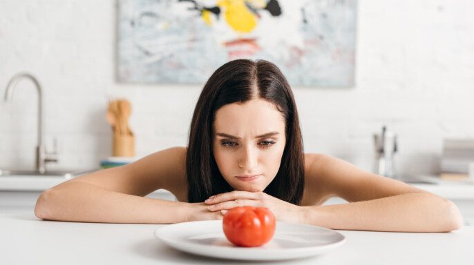 Chica pensativa mirando tomate maduro en la mesa de la cocina