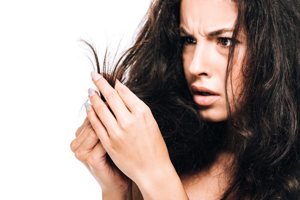 Mujer estresada mirando el cabello seco dañado