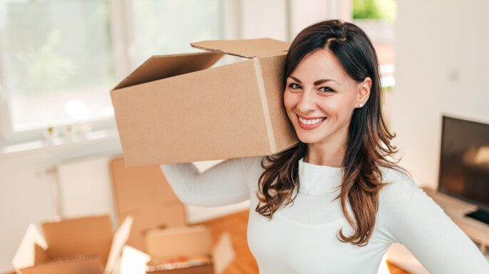Alegre mujer latina sosteniendo cajas mientras se mueve en nueva