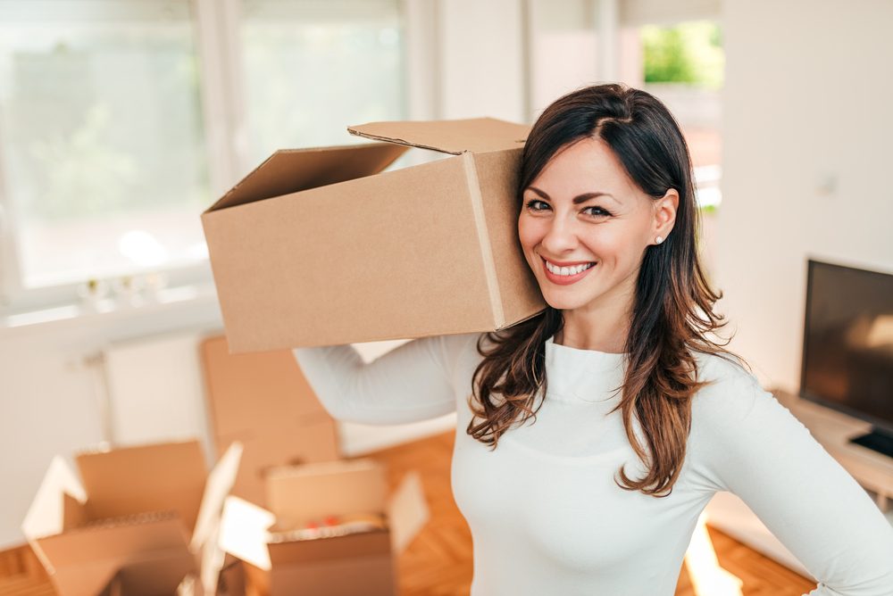 Alegre mujer latina sosteniendo cajas mientras se mueve en nueva