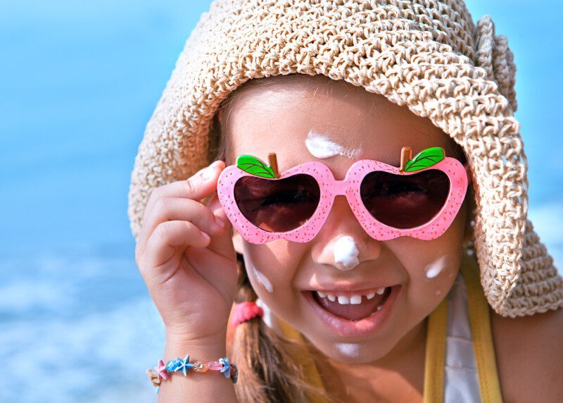 Niña feliz con gafas y protector solar en la cara