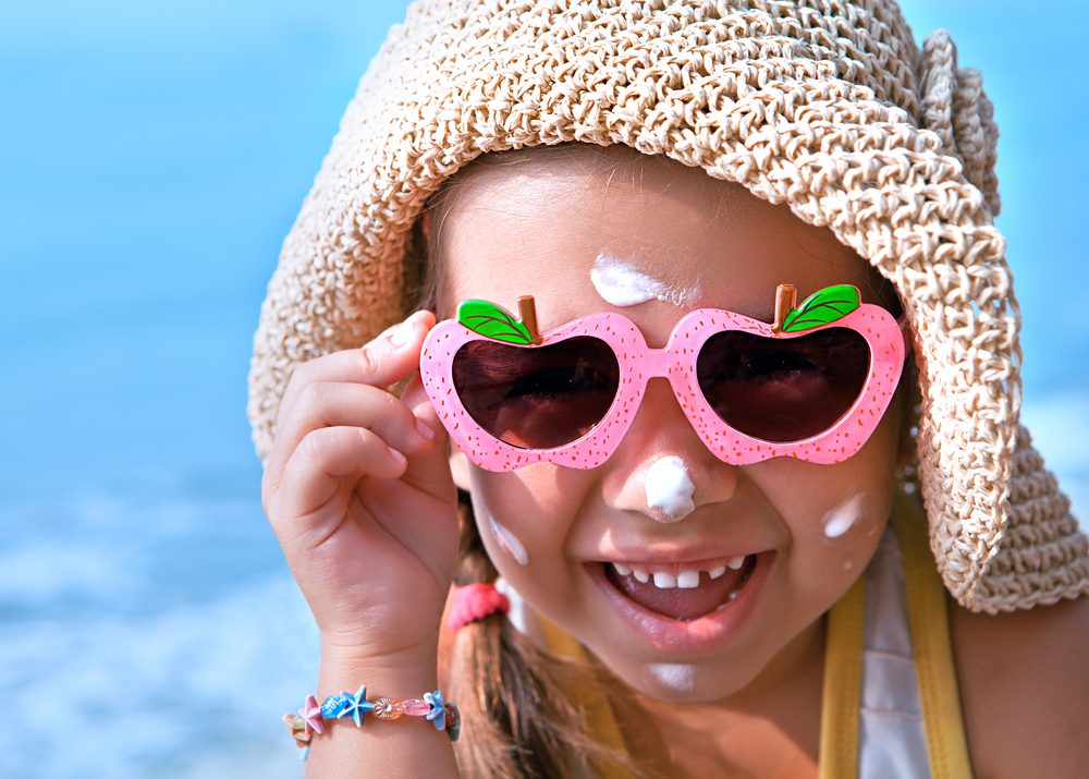 Niña feliz con gafas y protector solar en la cara