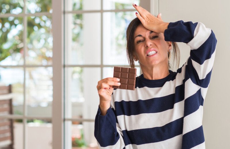 Mujer de mediana edad comiendo barra de chocolate estresada