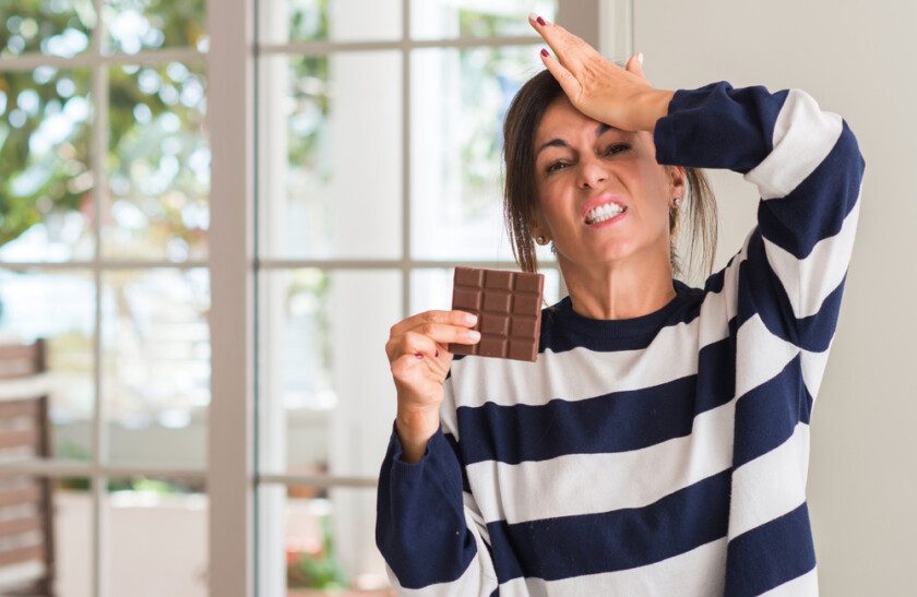 Mujer de mediana edad comiendo barra de chocolate estresada