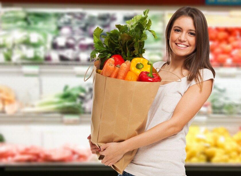 Mujer sonriendo con una bolsa de vegetales en un supermercado
