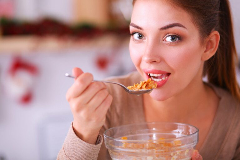 Mujer sonriente desayunando en el interior de la cocina