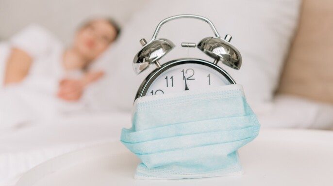 Enfoque selectivo de reloj despertador vintage envuelto en cubrebocas atrás una mujer en la cama