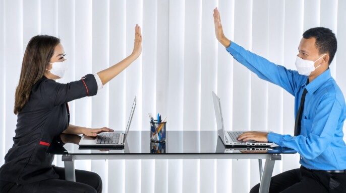 Dos personas de negocios con cubrebocas dando manos sin contacto mientras trabajan en la oficina en un nuevo estilo de vida normal
