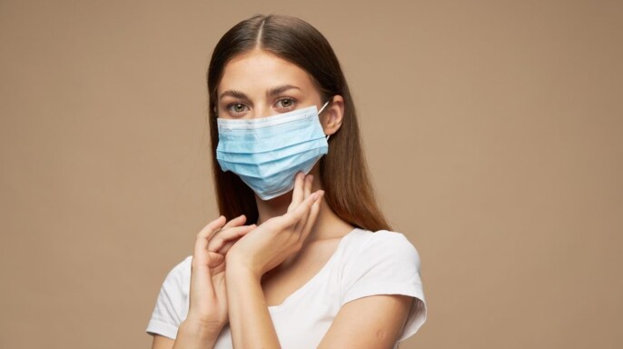 Mujer joven en máscara médica usando desinfectante de manos