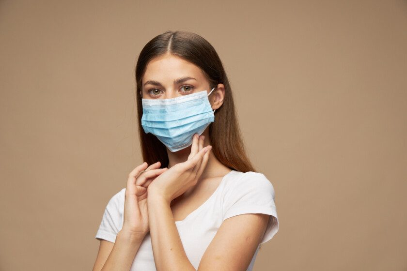 Mujer joven en máscara médica usando desinfectante de manos