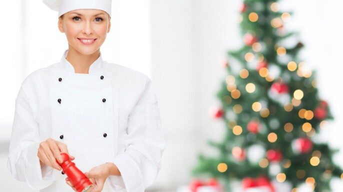 Chef sonriente especiando ensalada de verduras con árbol navideño al fondo