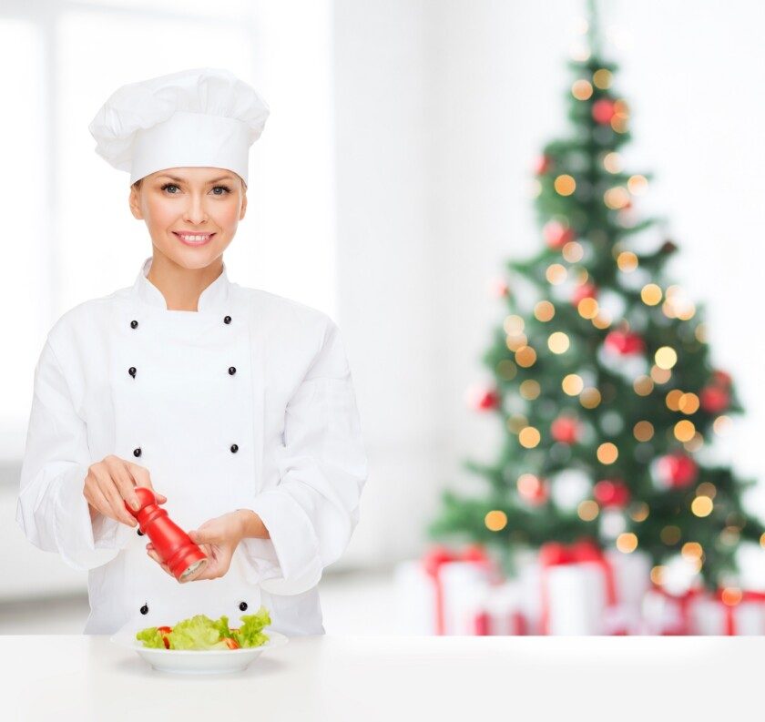 Chef sonriente especiando ensalada de verduras con árbol navideño al fondo
