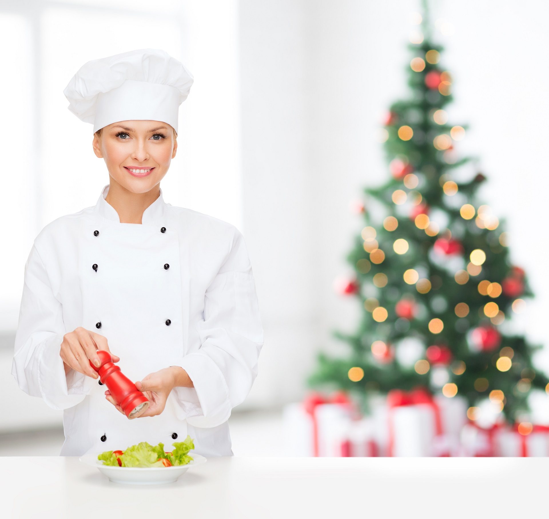 Chef sonriente especiando ensalada de verduras con árbol navideño al fondo