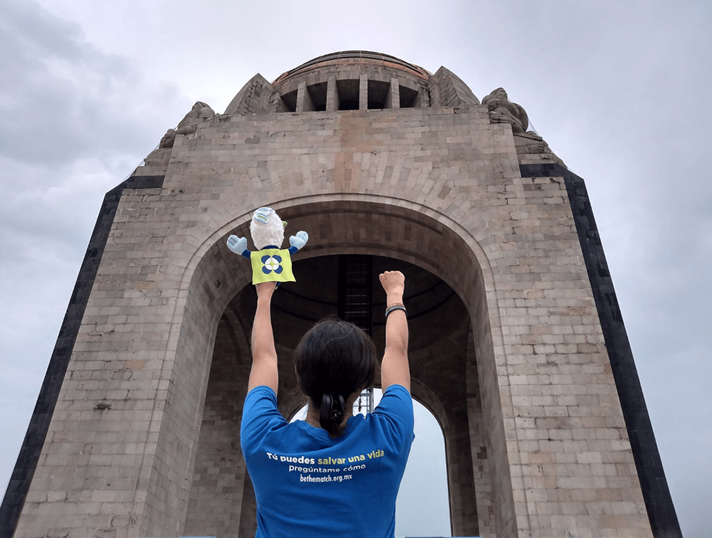 Persona de espaldas con las manos en alto mirando el monumento a la revolución