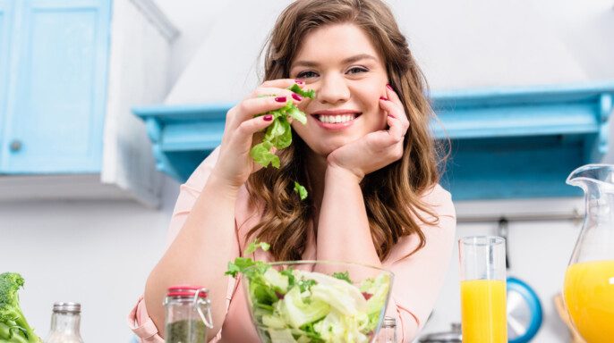 Mujer sonriente con sobrepeso en la mesa con ensalada fresca