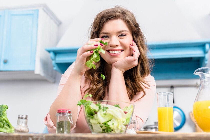 Mujer sonriente con sobrepeso en la mesa con ensalada fresca