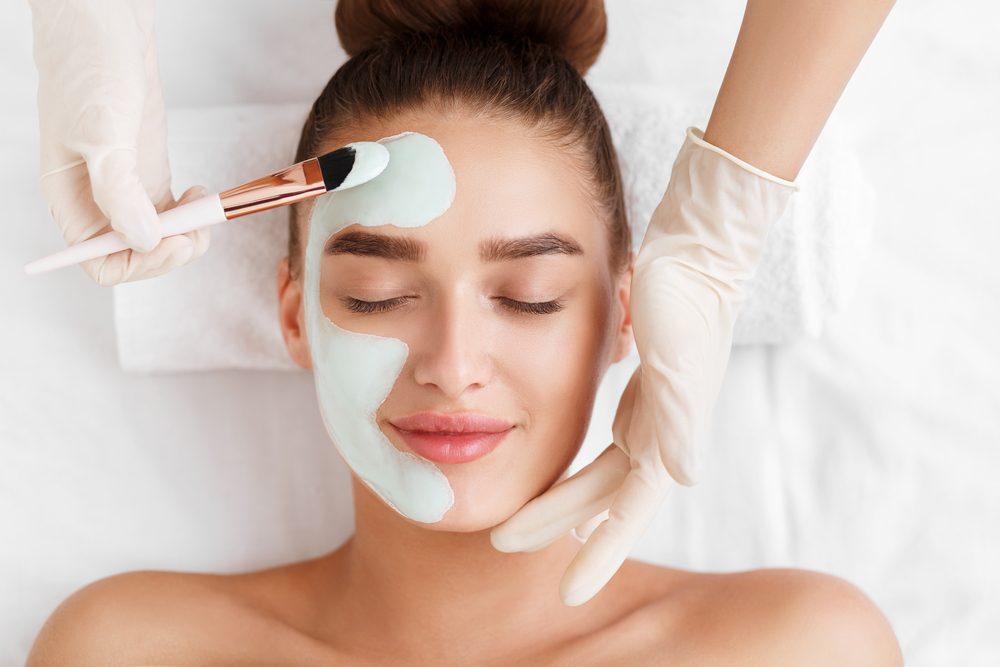 Esteticista aplicando mascarilla de arcilla en la cara de mujer