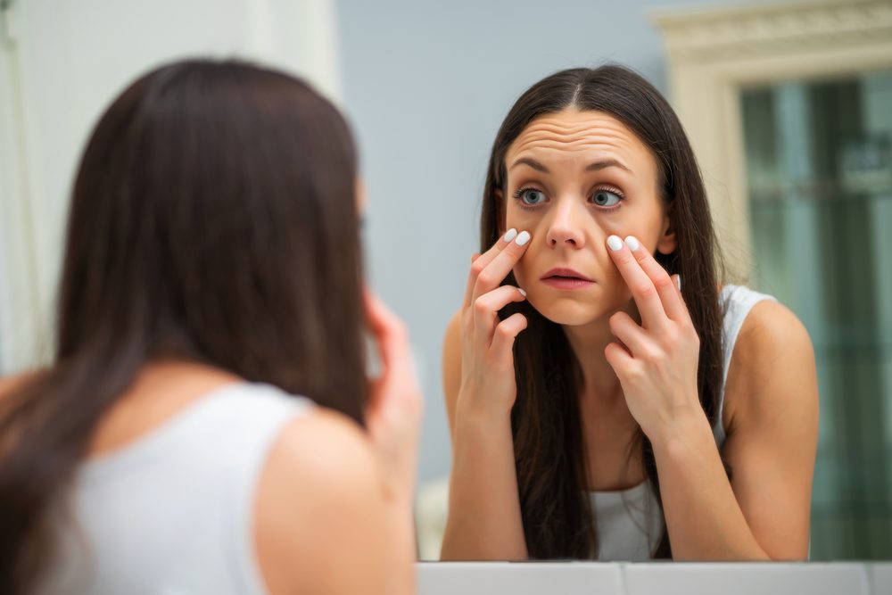 Mujer cansada mirando sus bolsas de ojos en el baño