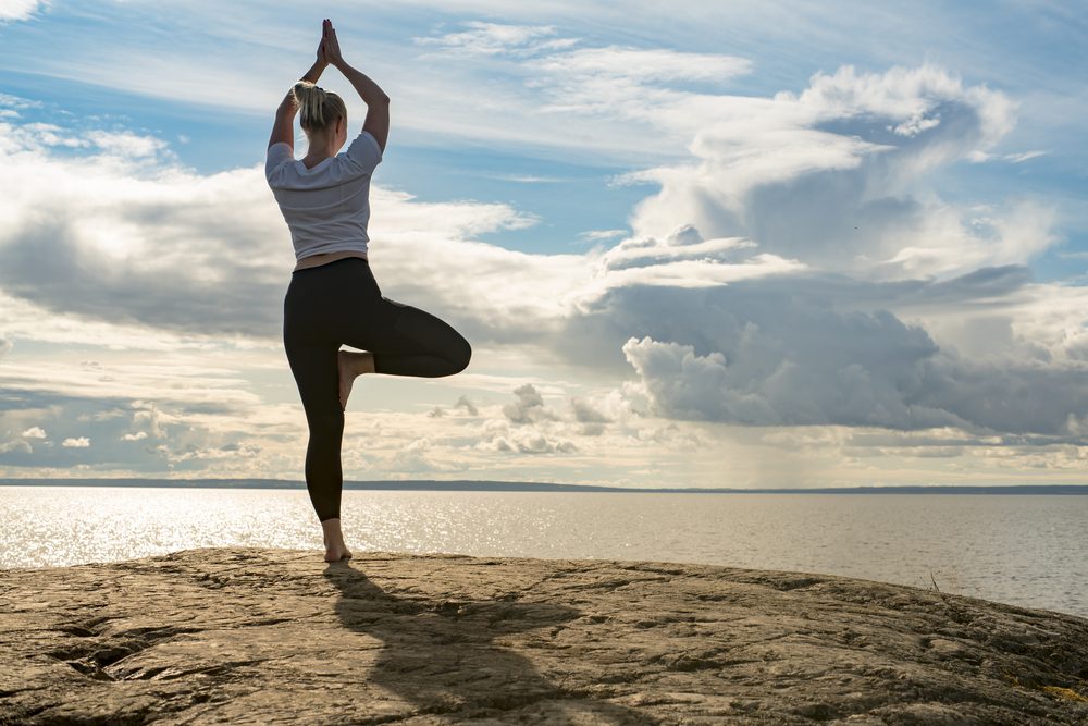 Mujer haciendo yoga mirando al océano en una playa