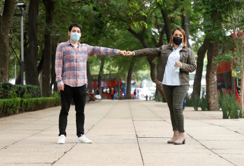 Dos personas con puños cerrados extienden brazos para mantener sana distancia
