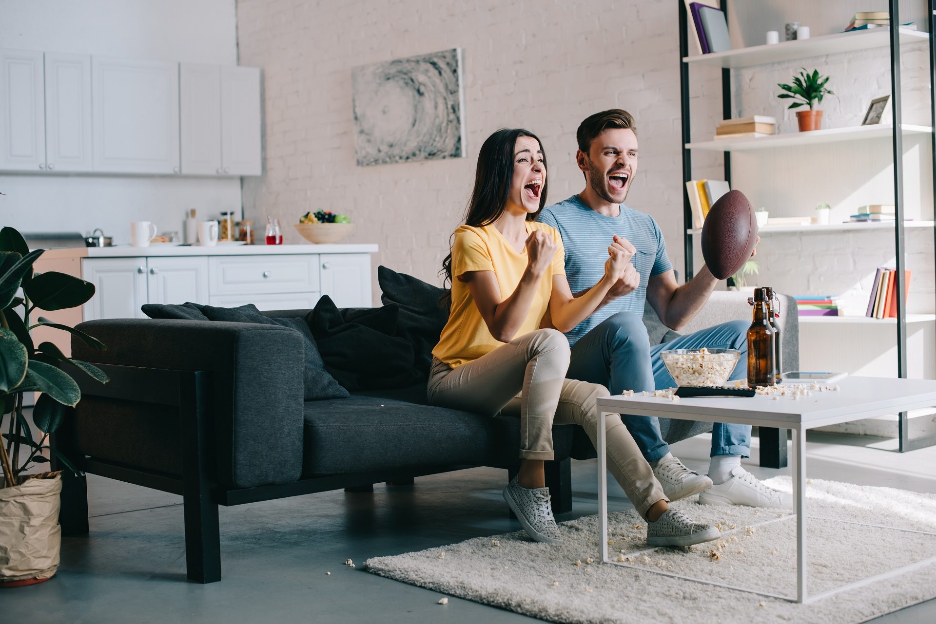 Pareja joven expresiva animando para el partido de fútbol americano en casa