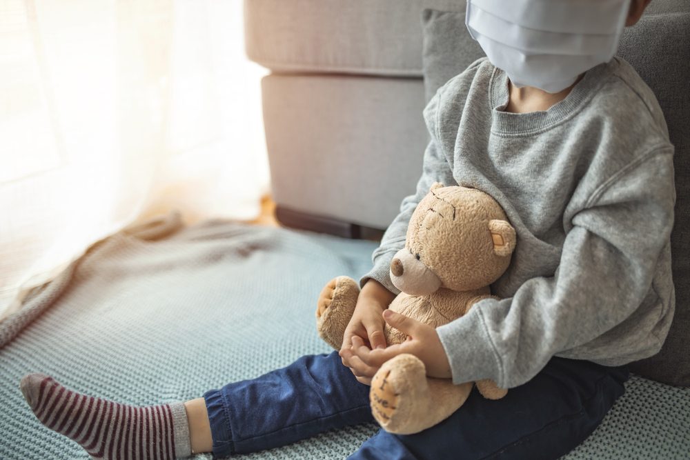 Niño en cuarentena en casa jugando en la ventana con su oso de peluche