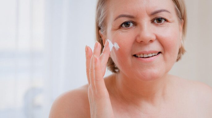 Mujer mayor sonriente aplicando loción antienvejecimiento para el rostro
