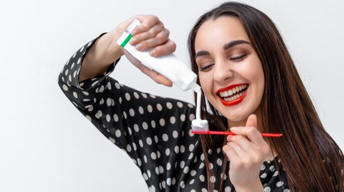 Mujer joven sosteniendo un cepillo de dientes y colocando pasta dental