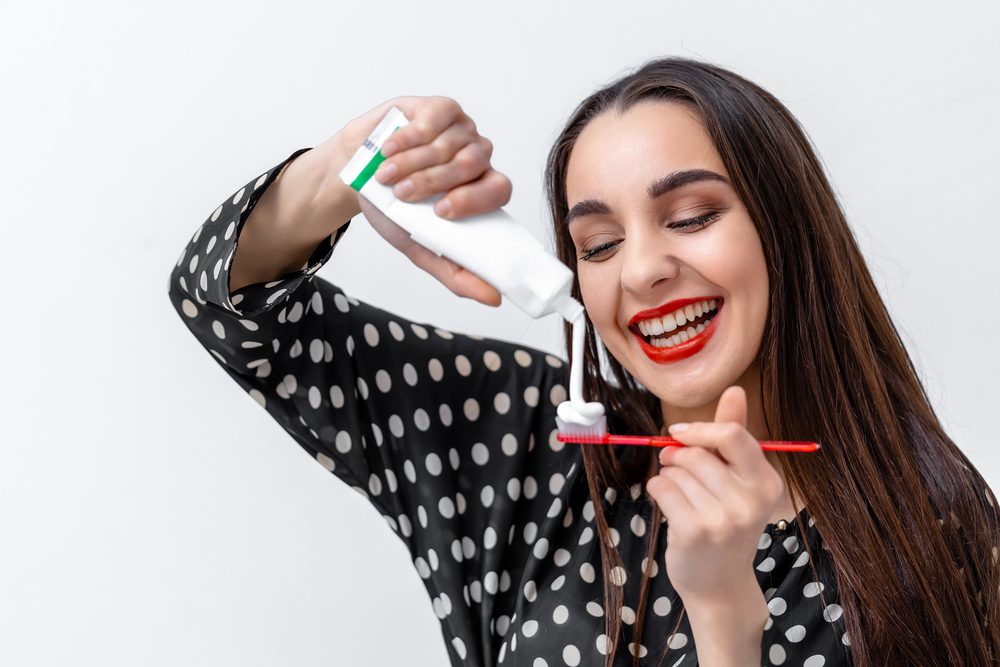 Mujer joven sosteniendo un cepillo de dientes y colocando pasta dental