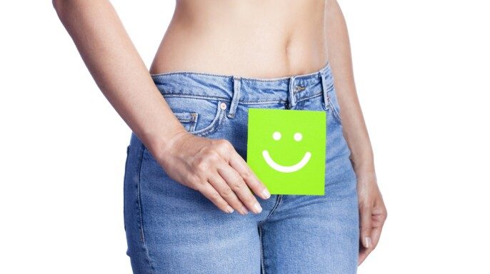 Mujer sosteniendo pagina cuadrada chica verde con icono de feliz enfrente de sus jeans
