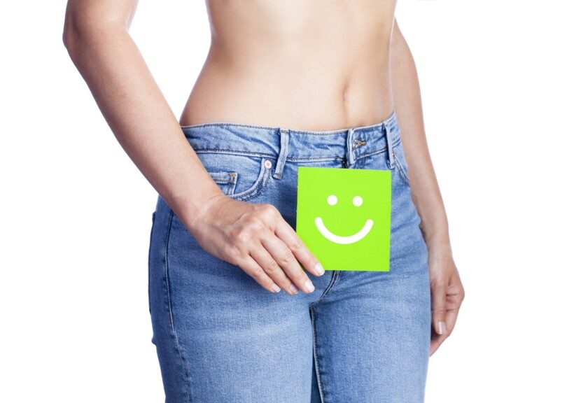 Mujer sosteniendo pagina cuadrada chica verde con icono de feliz enfrente de sus jeans