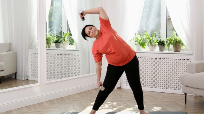 Mujer madura con sobrepeso haciendo ejercicio con pesas en cas
