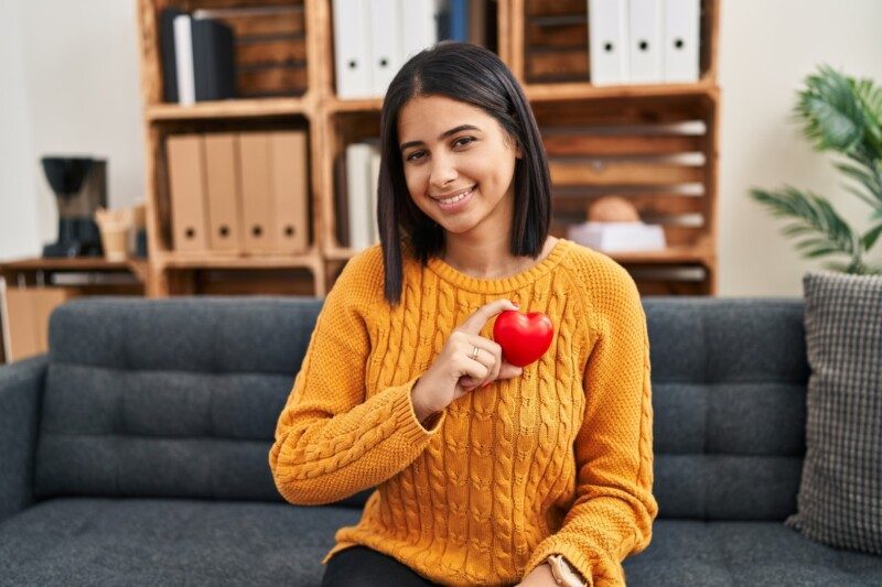 Joven paciente sonriendo confiada sosteniendo un corazón de juguete